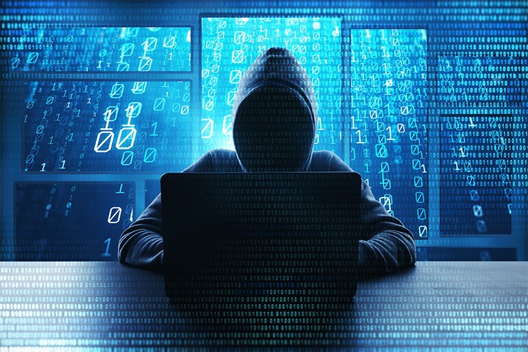 A hacker with a hoodie sitting with a laptop with 0 and 1s background.